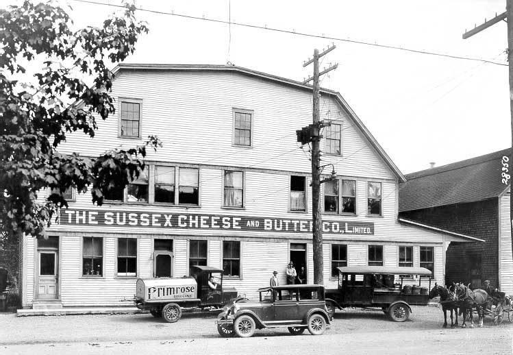 A milk delivery truck full of milk cans sits in front of the Sussex Cheese and Butter Co., Limited
