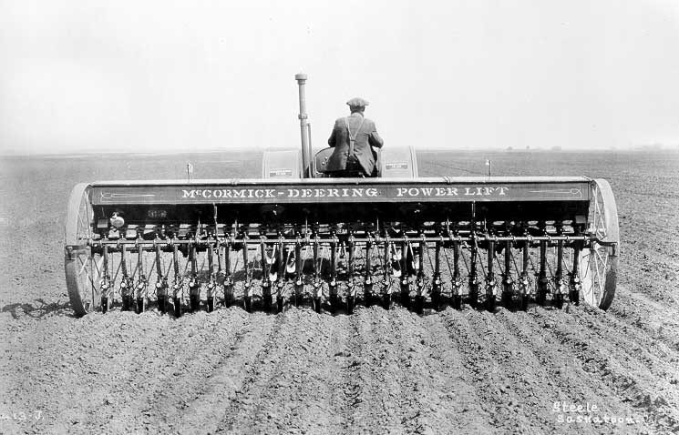 Farmer sowing seeds with a 28-row disk drill pulled by a McCormick Deering 15-30 tractor