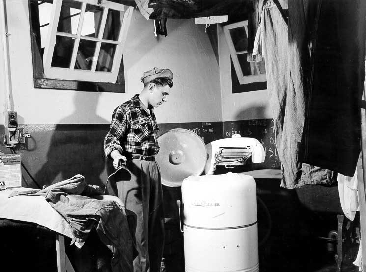 A young man irons and checks a wash in the YMCA laundry facilities