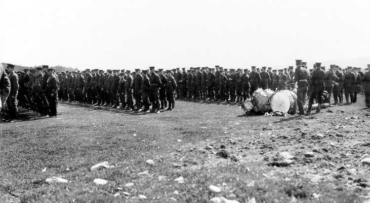 Soldiers lined up at a WWI training camp with marching band instruments beside them