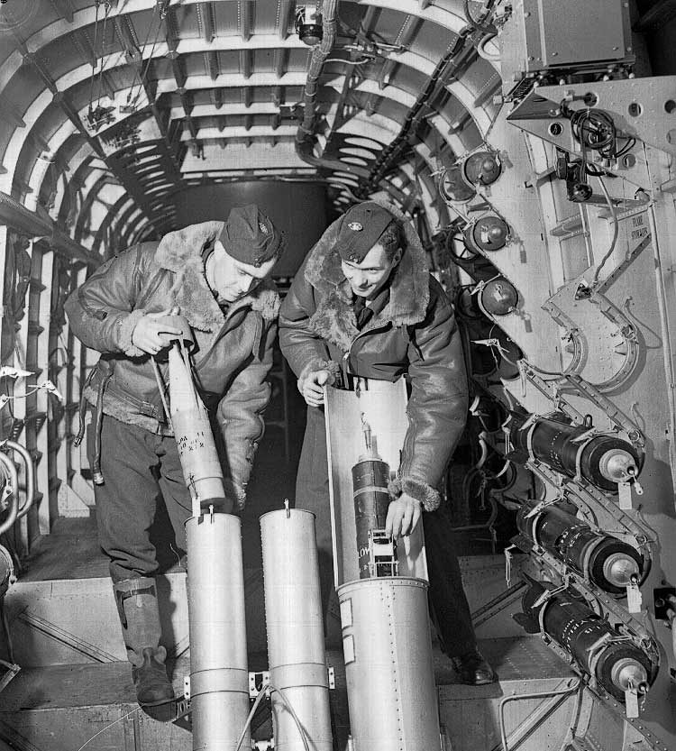 Two RCAF crew members place flares in the flare chute of a Stirling bomber to light up their targets