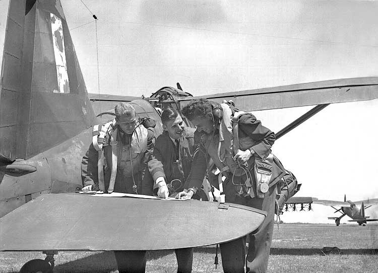 Three Royal Canadian Air Force Army Cooperation Squadron pilots scan a map before take-off