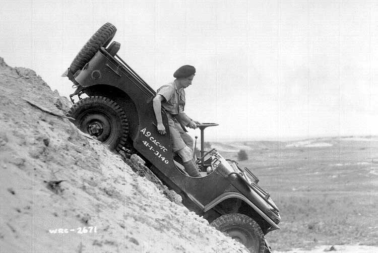 An Armoured Corps jeep containing two soldiers makes its way down a steep hill