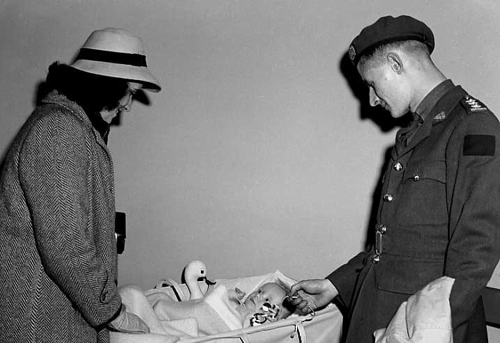 A war bride watches her child's reaction as a soldier plays with the baby in Central Station