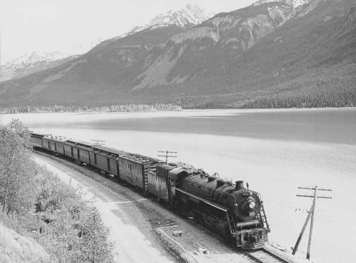Canadian National Railways steam locomotive no. 6044 hauls a passenger train beside a lake west of Jasper