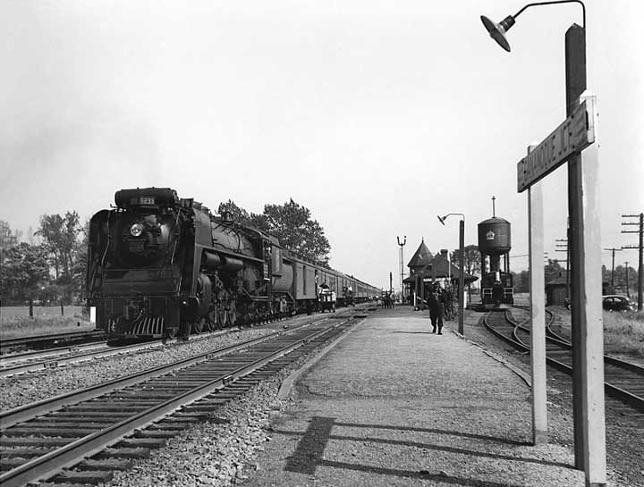 A Canadian National Railways passenger train hauled by steam locomotive no. 6233 takes on baggage and supplies at a railway station