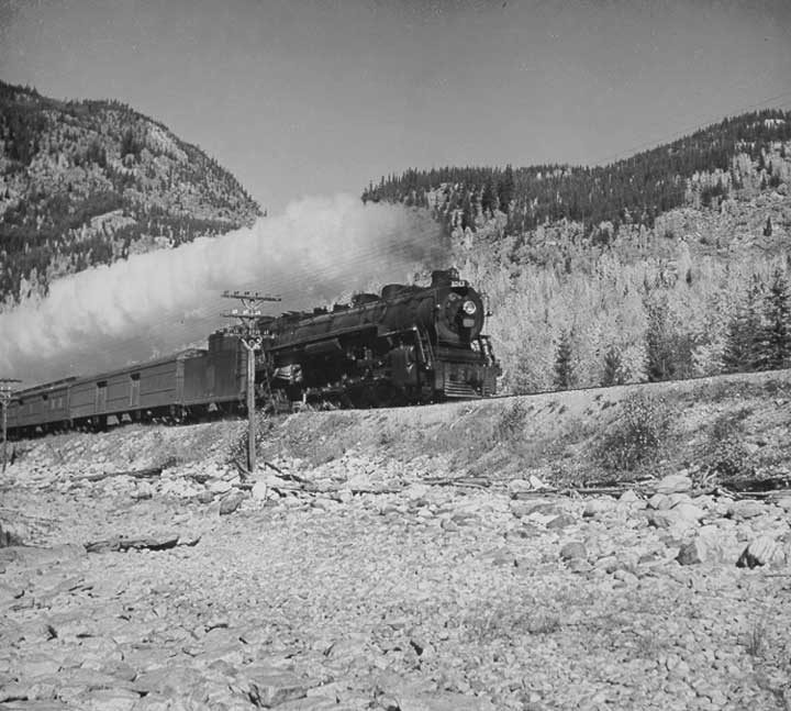 Canadian National Railways steam locomotive no. 6043 hauls a passenger train through the foothills