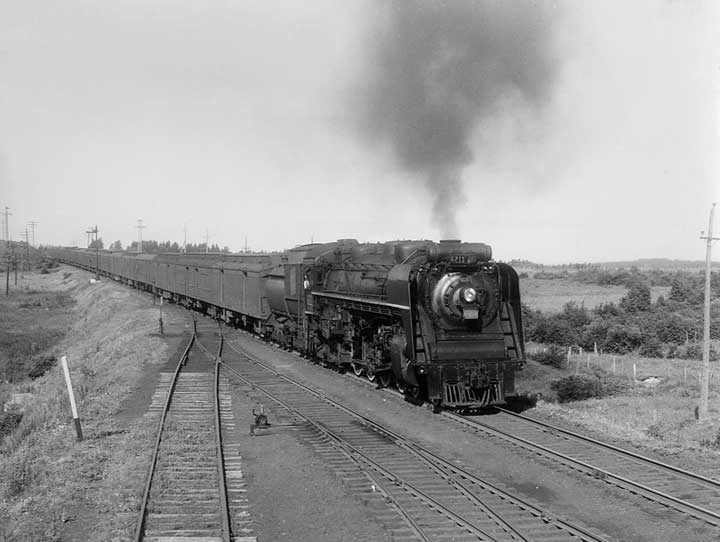 A Canadian National Railways passenger train, hauled by steam locomotive no. 6211, pulls toward a railway station