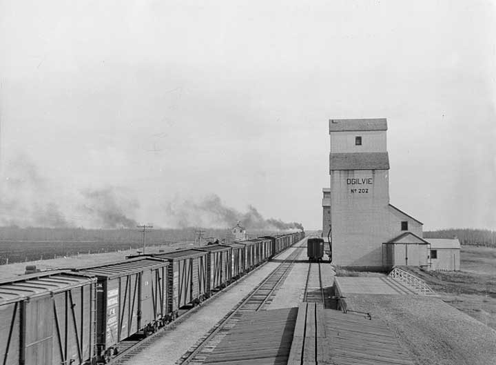 A freight train hauls grain past an elevator toward the head of the Great Lakes