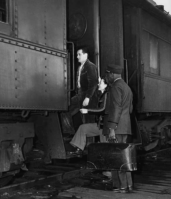 A porter helps a young immigrant couple to board a passenger coach