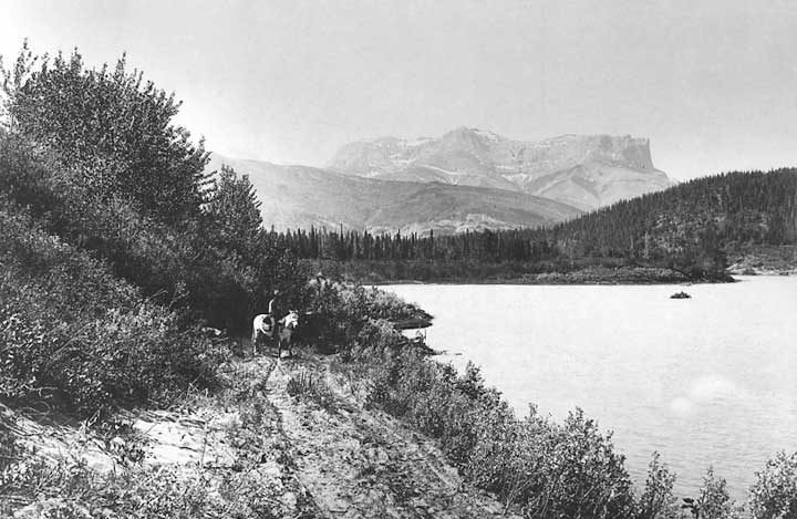 A man rides a pack horse beside Brûlé Lake