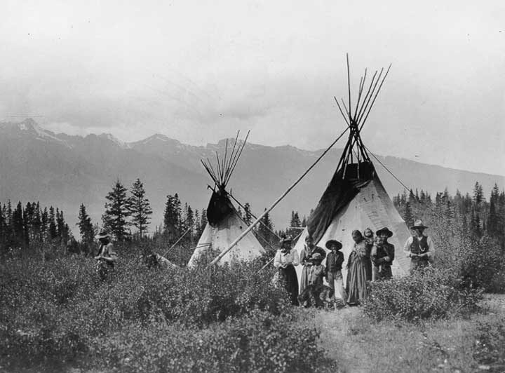 Shuswap families with children and a dog, outside two teepees.
Original caption: