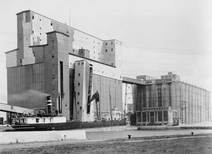 A small cargo ship transfers cargo at a grain elevator