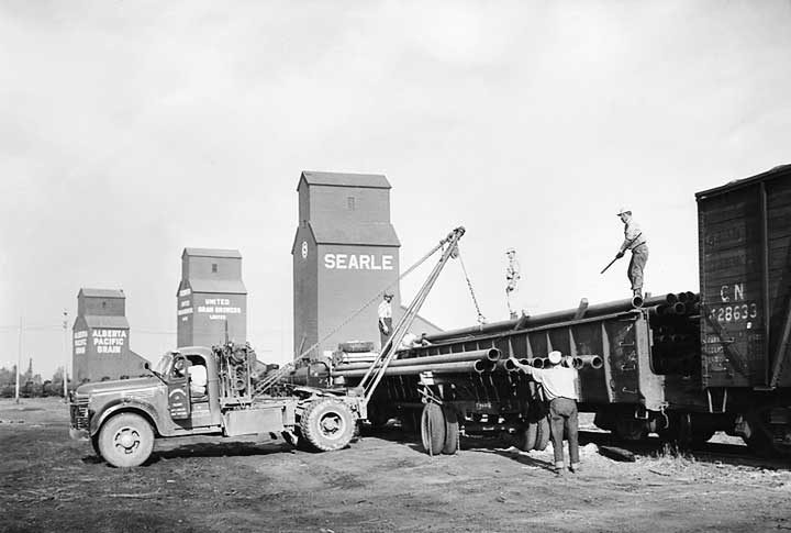 A car load of pipes is unloaded to be transported to the oil fields
