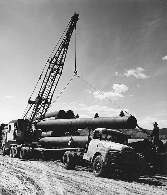Crane unloading pipe segments from a flatbed truck