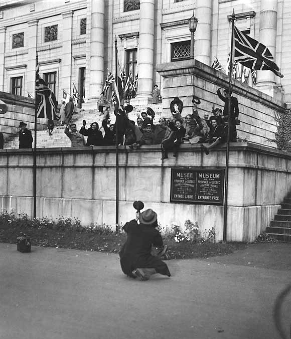 A photographer takes a picture of cheering well-wishers in front of the Museum of the Province of Québec as Princess Elizabeth and the Duke of Edinburgh approach