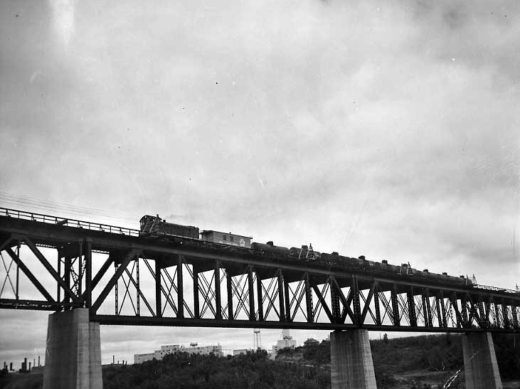 CNR diesel hauling tank cars over bridge near Edmonton, Canadian Chemicals Plant in rear