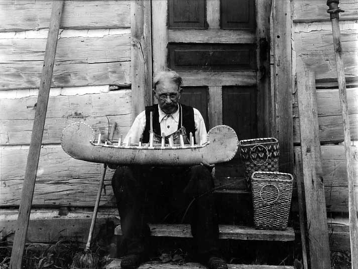 Ojibway Elder crafting a model of a birch bark canoe at Sheedy Camp, French River