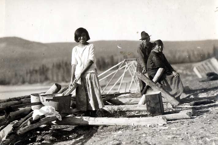 Outdoor scene of girl at wash board, as Elderly couple look on. 
Original caption: