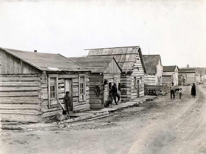 Aboriginal villagers outside a row of wooden homes.
Original caption: