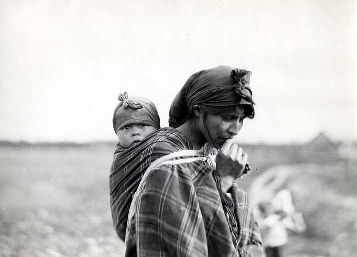 Woman in plaid shawl, carrying baby strapped to her back