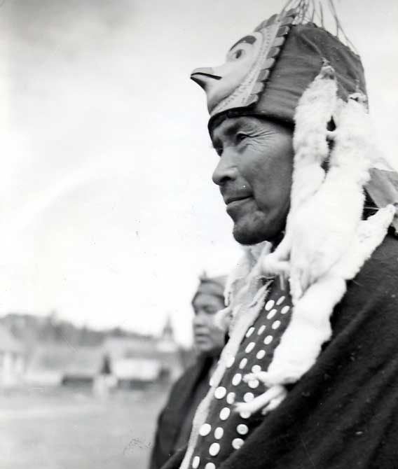 Wet'suwet'en man wearing bird head piece with ermineskin fringe and button blanket.
Original caption: