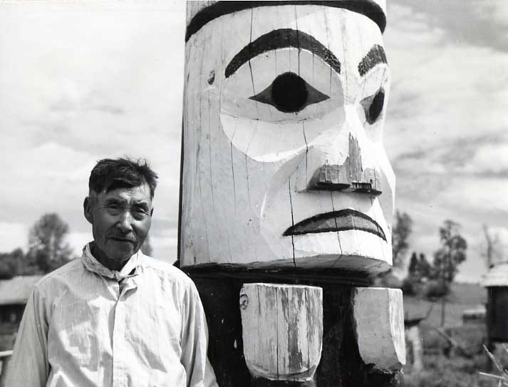 Donald Gray in front of aged, painted totem pole.
Original caption: