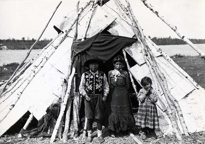 Ojibwa boy and two grils at the entrance to their birch bark wigwam. 
Original caption: