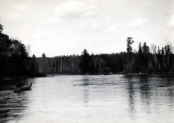 Ojibwa man paddling across a lake in a birch bark canoe.
Original caption: