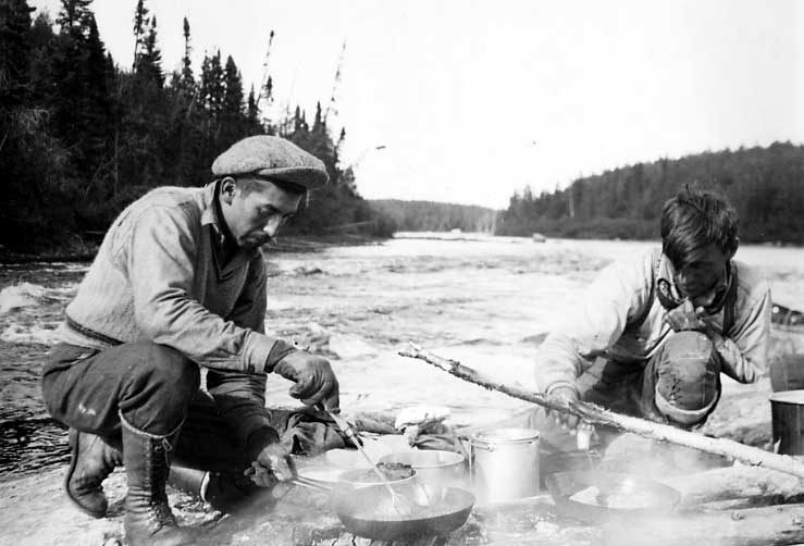 Two Ojibwa men preparing a shore lunch along the Ogoki River.
Original caption: