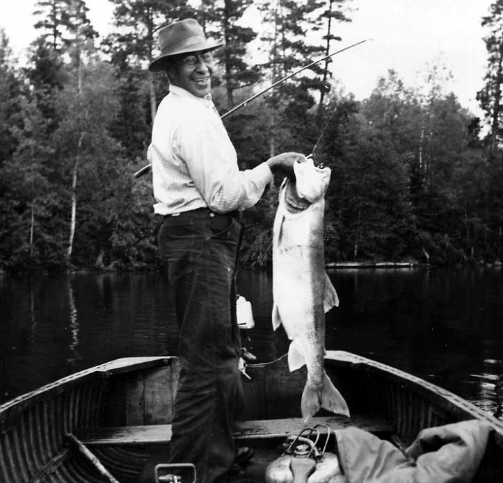 Ojibwa man standing in canoe displaying salmon trout catch of the day
