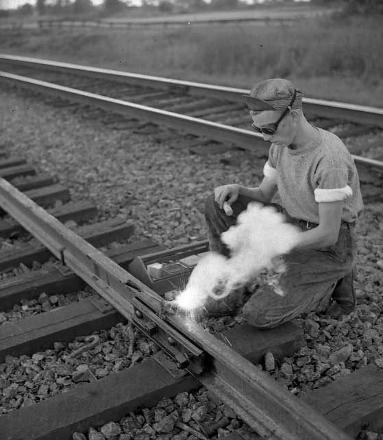 Bonding a new rail line.  A signal department employee connects rails by a short length of steel to ensure good electrical contact for train detection.