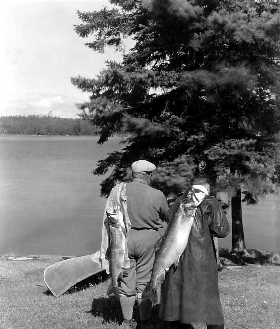 Two Ojibwa men walking away with trout over their shoulders.
Original caption: