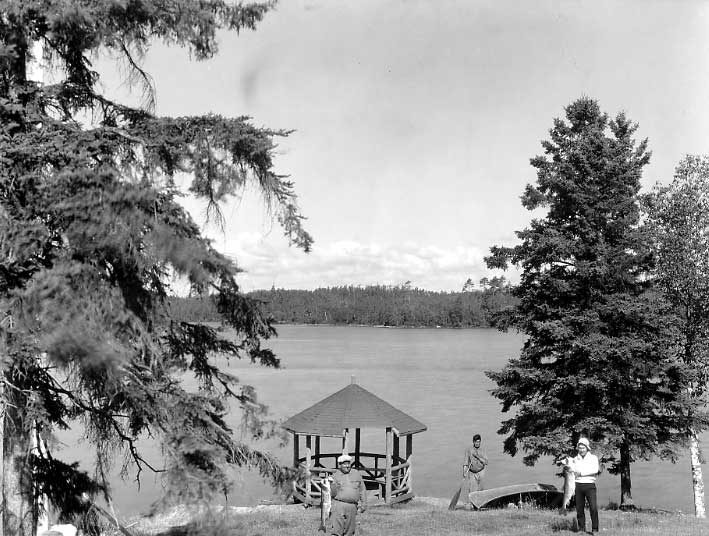 Three Ojibwa men at shore with fish and canoe