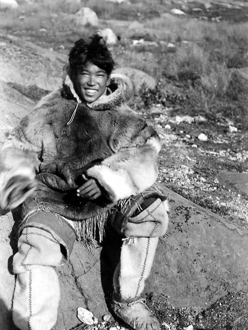 Inuk boy in traditional clothing, seated on rocks