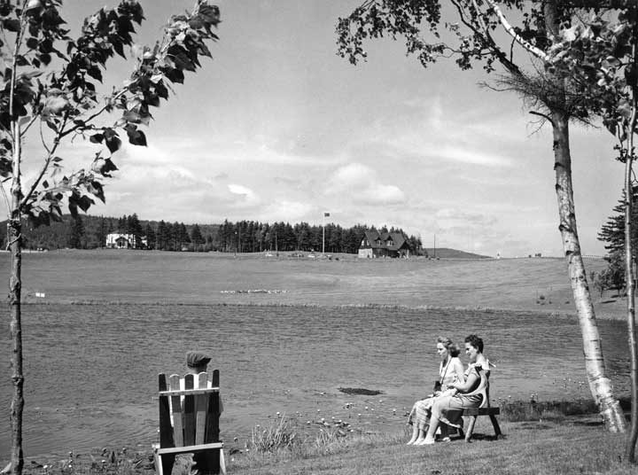 Tourists resting near Maclaren Pool, with Administration Building in the background, Fundy National Park