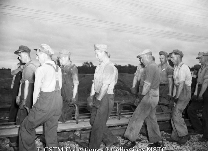 Tong men, ten at each side, lift the 39-foot, 1033 pound rail into place