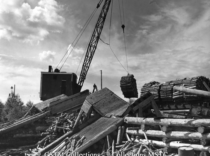Bundles of wood being lifted from rail cars into the water