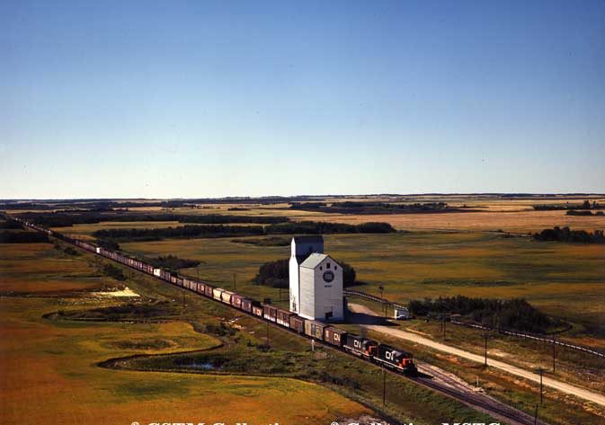 Freight train passing a grain elevator with a crib annex at Smart, Manitoba