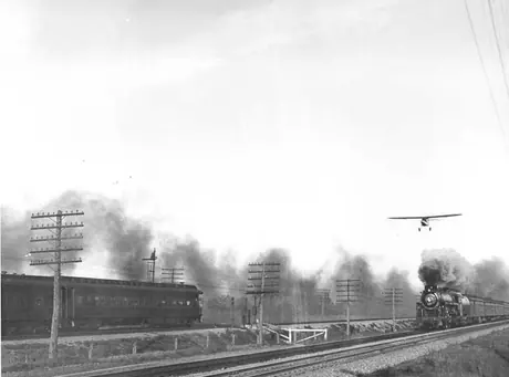 An airplane overflying a steam locomotive