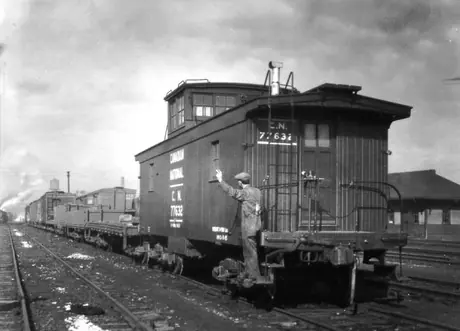 Train crew member giving a go-ahead hand signal from the steps of a caboose