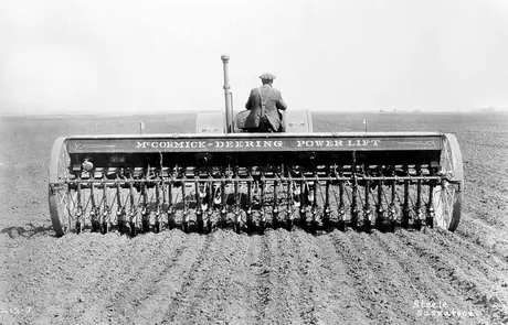 Farmer sowing seeds with a 28-row disk drill pulled by a McCormick Deering 15-30 tractor