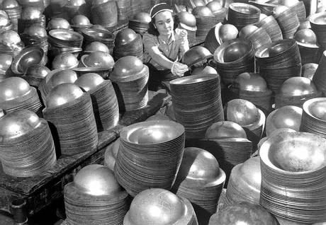 Women worker sitting amongst stacks of steel helmets at General Steel Wares