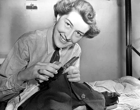 An RCAF Women's Division airwoman polishes her uniform buttons using a button stick before a parade