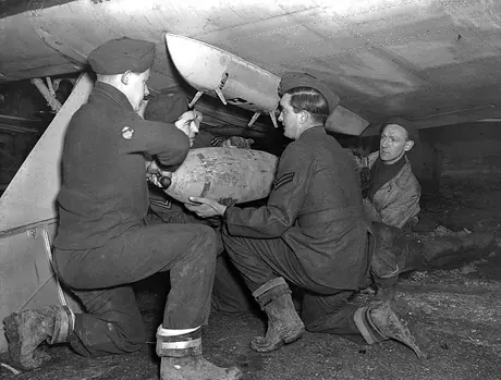 Four RCAF members affix a fused bomb to a Hurricane bomber's bomb rack at an RCAF Bomber Squadron