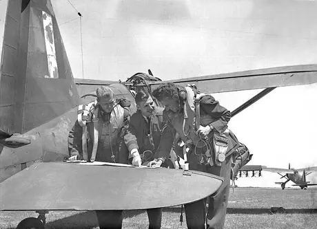 Three Royal Canadian Air Force Army Cooperation Squadron pilots scan a map before take-off