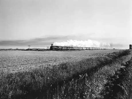A Canadian National Railways passenger train races past a distant wheat elevator on the prairies