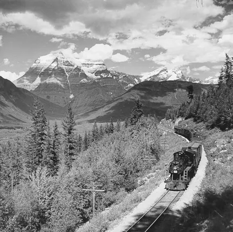 A Canadian National Railways freight train steams through the Rockies; telegraph lines run parallel to the track