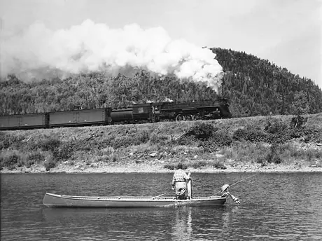 A fisherman watches Canadian National Railways steam locomotive no. 6181 steam by