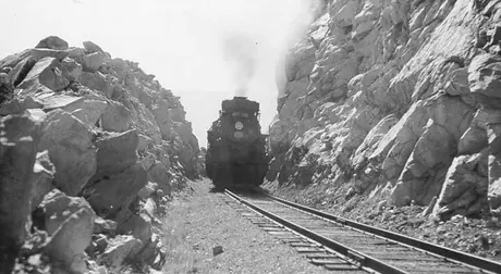 A Canadian National Railways steam locomotive steams through a mountain pass